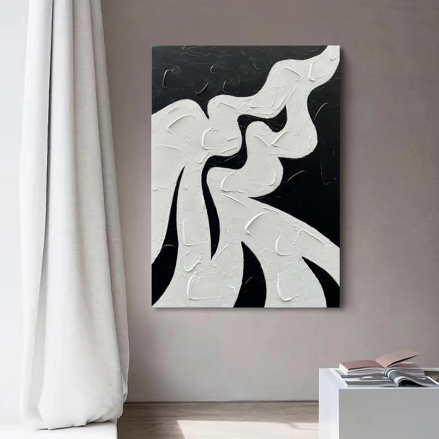 Abstract black and white artwork on a wall with a curtain and table in the foreground.