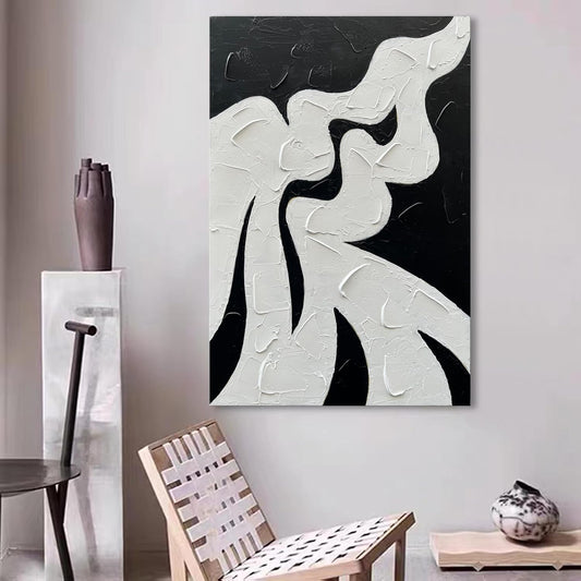 Abstract black and white painting on a wall with a chair and table in the foreground.