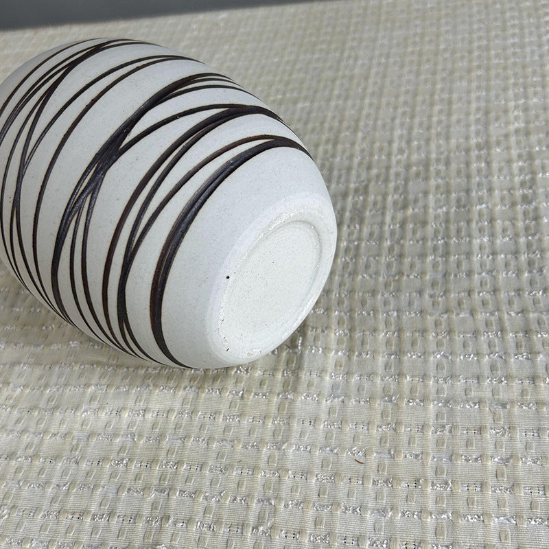 White cylindrical object with black stripes on a textured beige surface