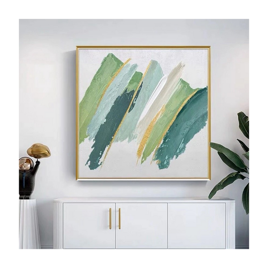 Abstract art print with green and gold brush strokes in a gold frame on a white wall.