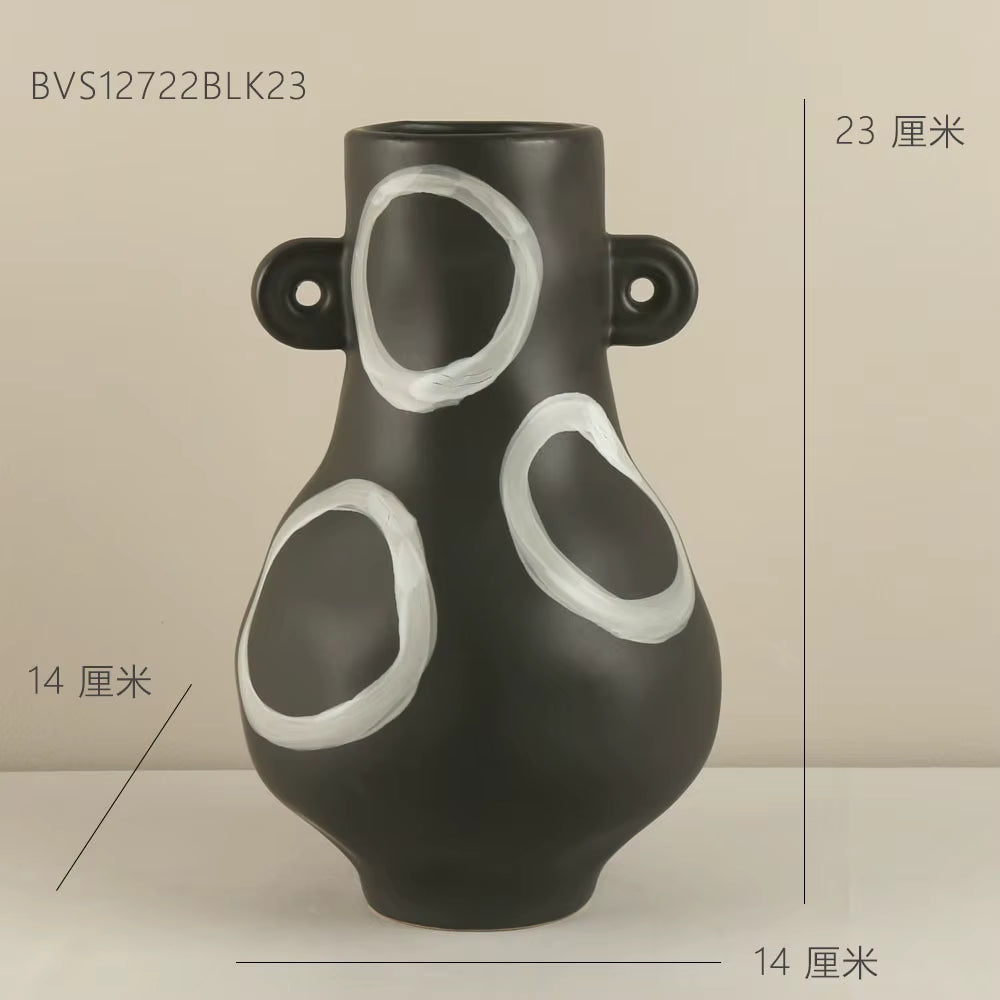 Black vase with white circular designs on a beige background
