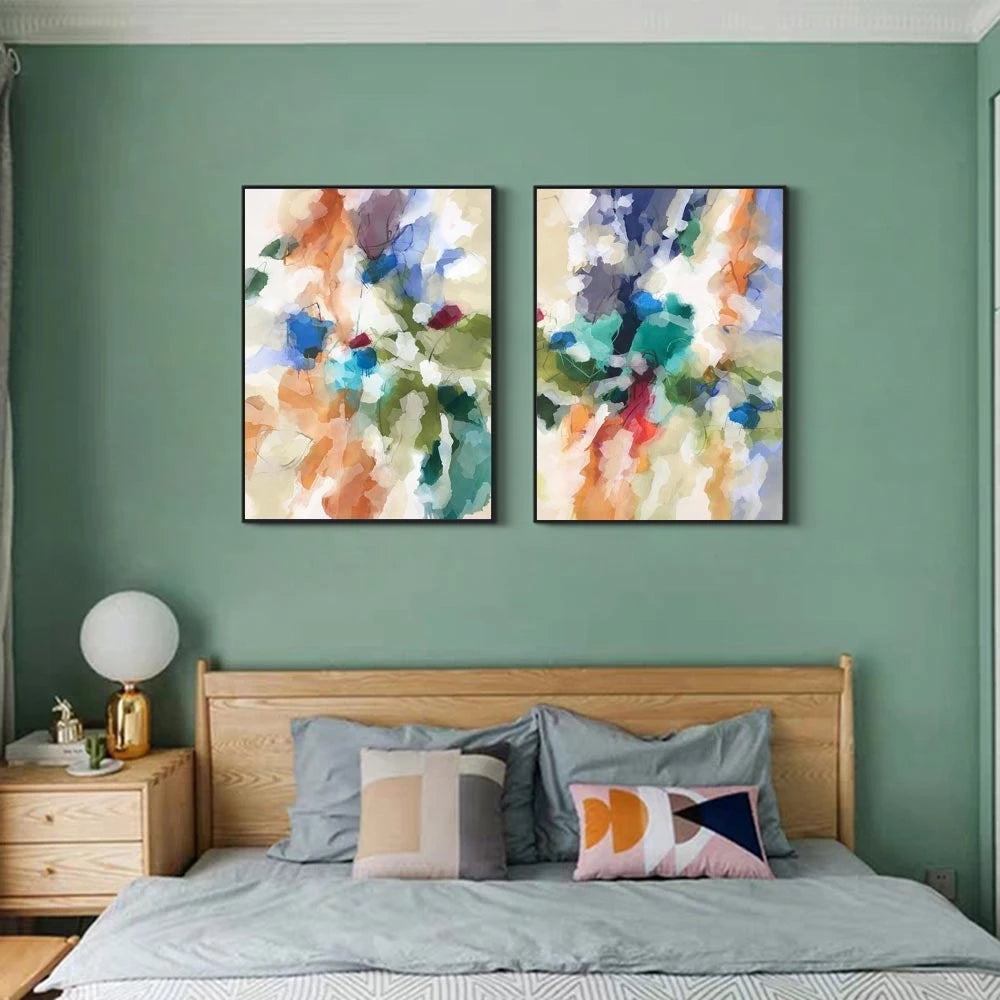 Two abstract paintings on a green wall above a bed with colorful pillows.