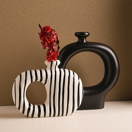 Black and white striped vase with red flowers next to a black vase on a brown background