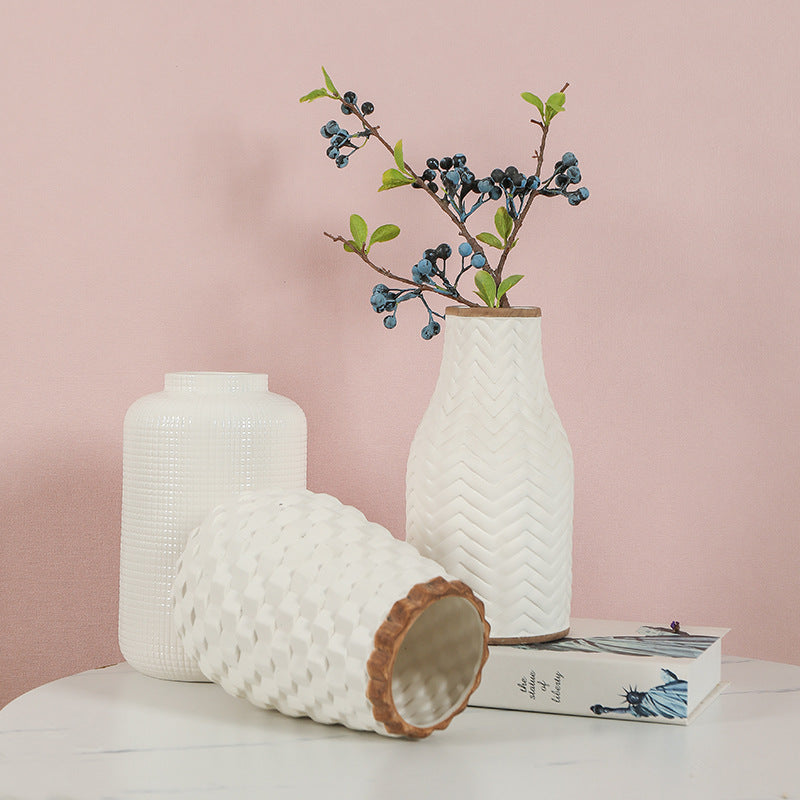 Two textured vases with wooden bases on a light surface against a pink background