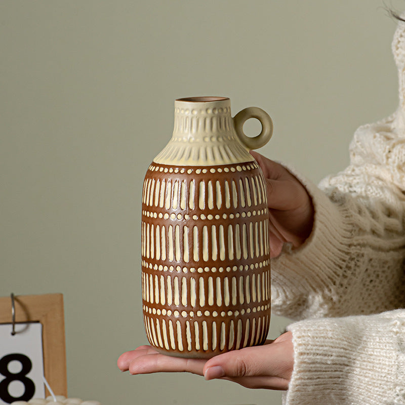 Person holding a ceramic vase with a patterned design against a neutral background