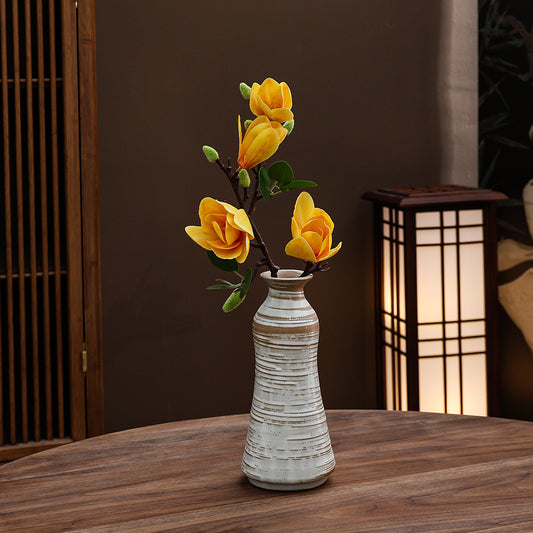 White ceramic vase with yellow flowers on a wooden table, with a blurred background