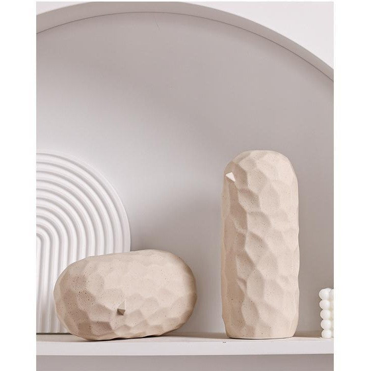 Two beige stone sculptures on a white shelf with a neutral background