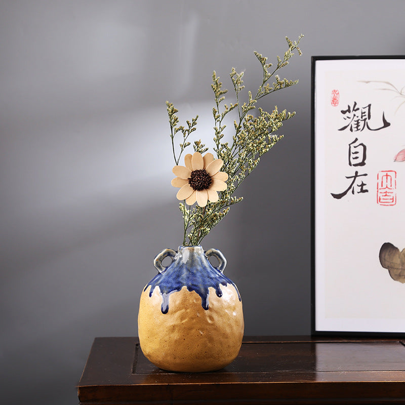 Decorative vase with flowers on a wooden surface against a gray wall with a framed picture.