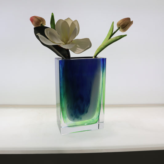 Glass vase with blue and green gradient holding flowers on a white surface.