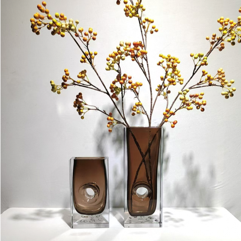 Two glass vases with decorative branches and berries on a white background