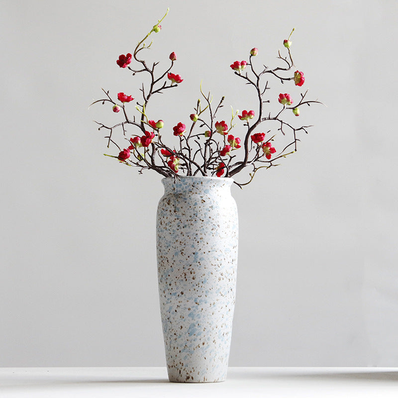 Speckled vase with red floral branches on a light gray background