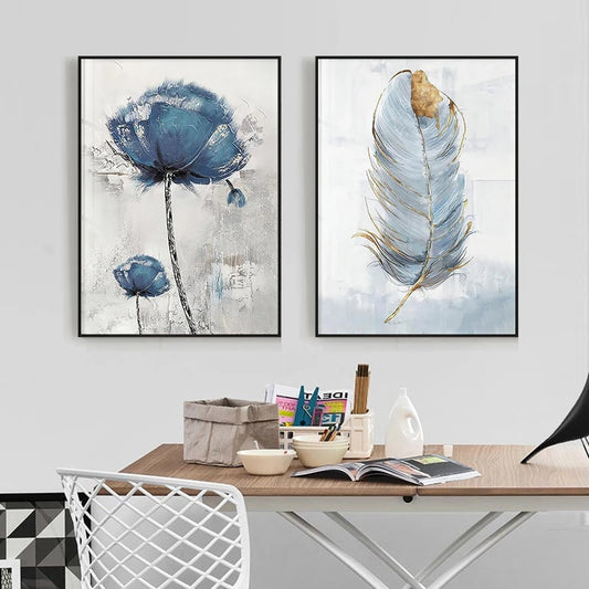 Two abstract art prints of blue flowers and feathers on a wall above a desk.