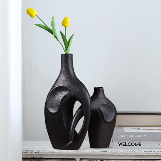 Two black ceramic vases with yellow tulips on a shelf.