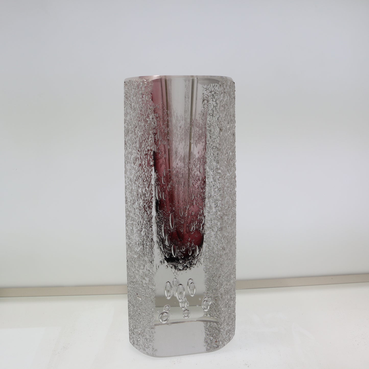 Cylindrical glass vase with textured surface and purple tint on a white background