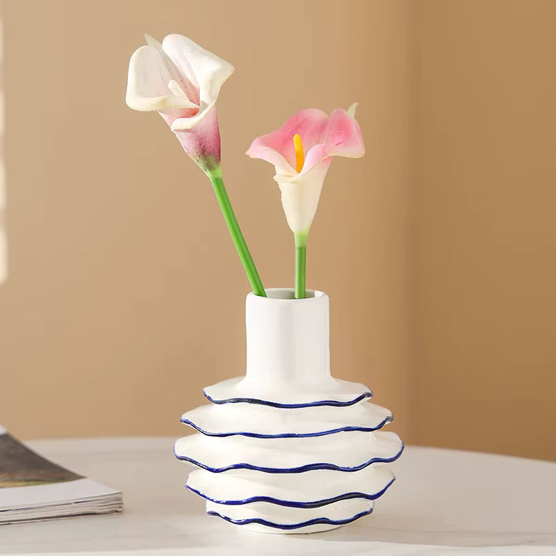 White vase with wavy design holding pink and white flowers on a beige background