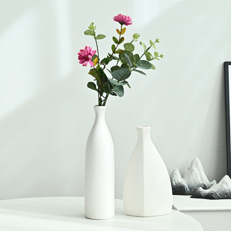 Two white vases with a single pink flower on a light surface against a plain background