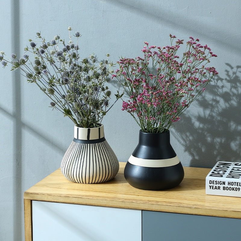 Two decorative vases with flowers on a wooden surface against a light blue wall.