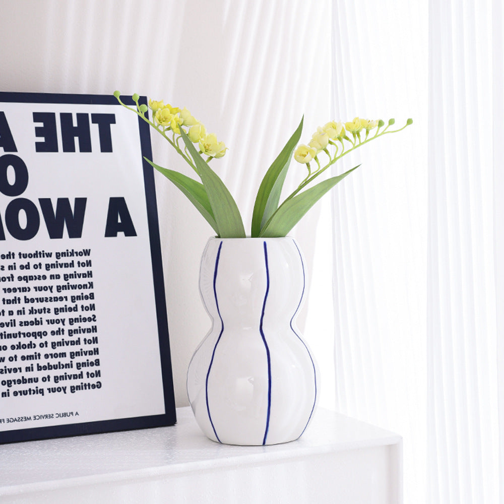 White vase with blue stripes containing yellow flowers on a white surface with a framed text poster in the background.