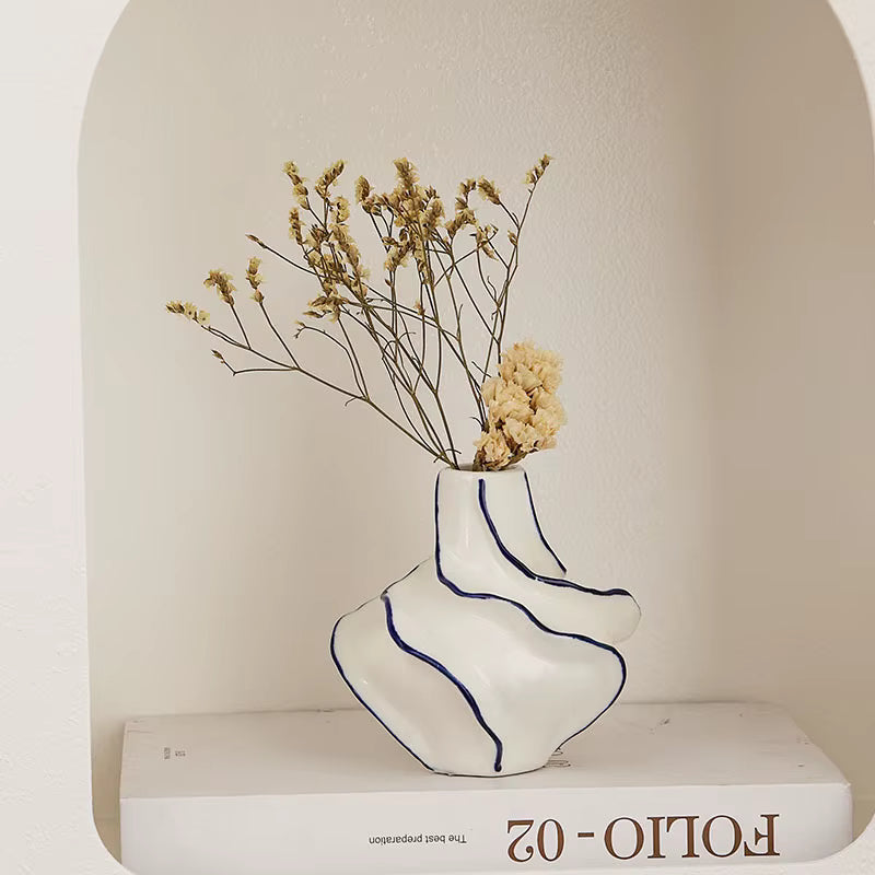 White vase with blue stripes containing dried flowers on a white surface with 'Folio-02' branding.