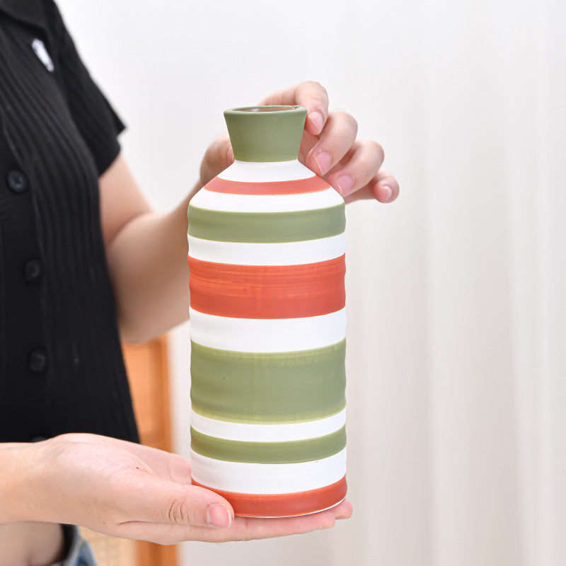 Person holding a striped ceramic vase with a plain background