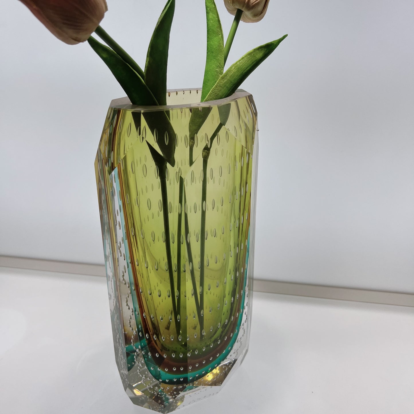 Glass vase with textured design containing green leaves on a white background