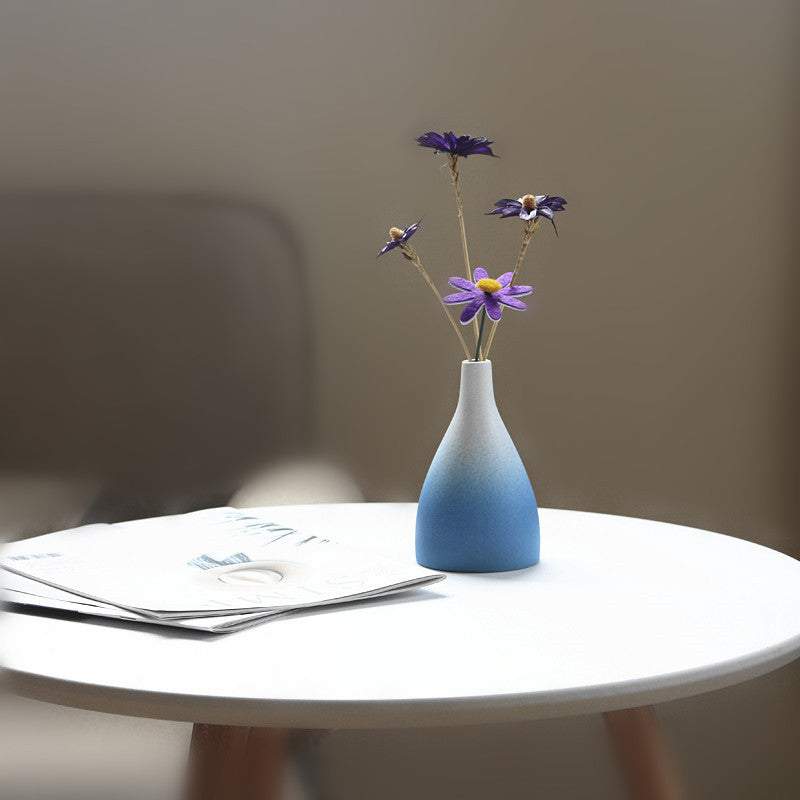 Blue vase with purple flowers on a white table against a blurred background