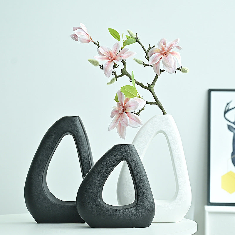 Two black ceramic vases with a white vase holding pink flowers on a light blue background.