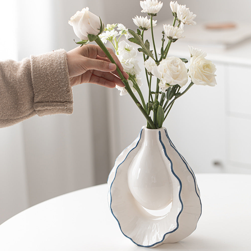Person arranging white flowers into a decorative vase on a table.