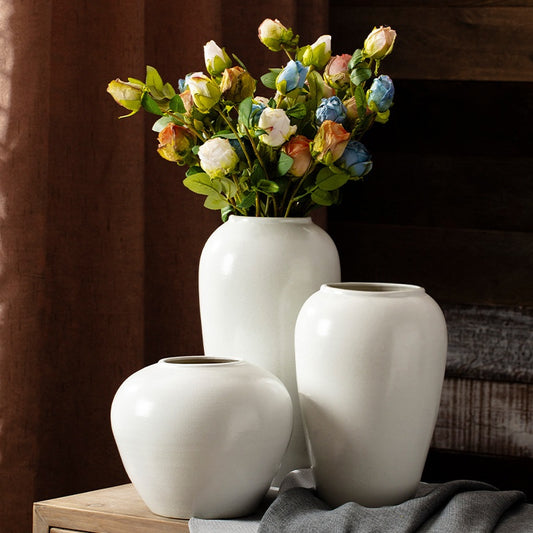 Three white vases with a bouquet of flowers on a wooden surface.