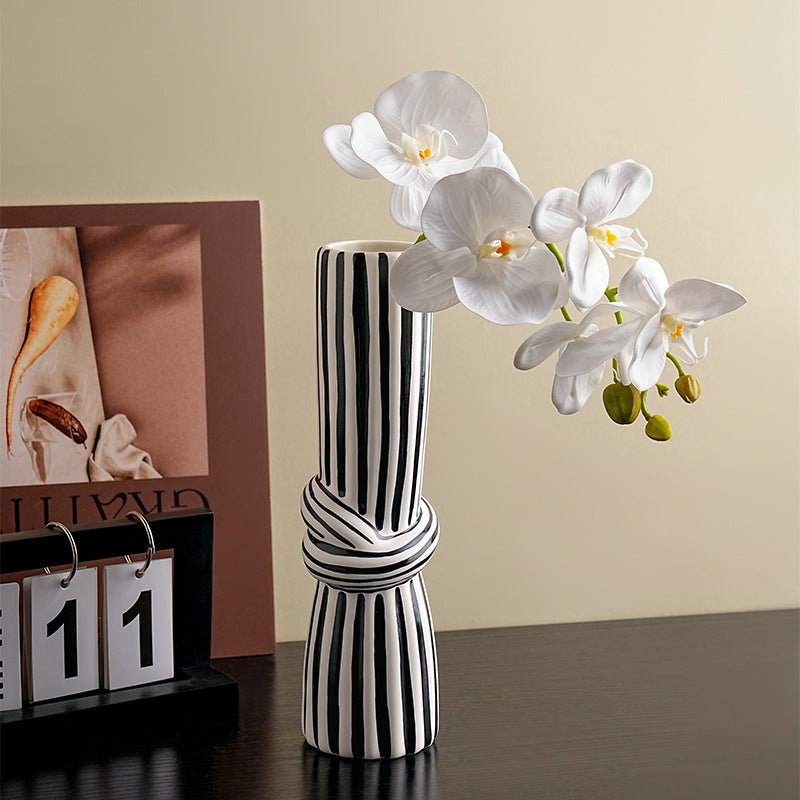 Black and white striped vase with a branch of white flowers on a table.