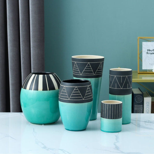 Set of teal and black patterned vases on a marble surface with a teal wall and gray curtain in the background.