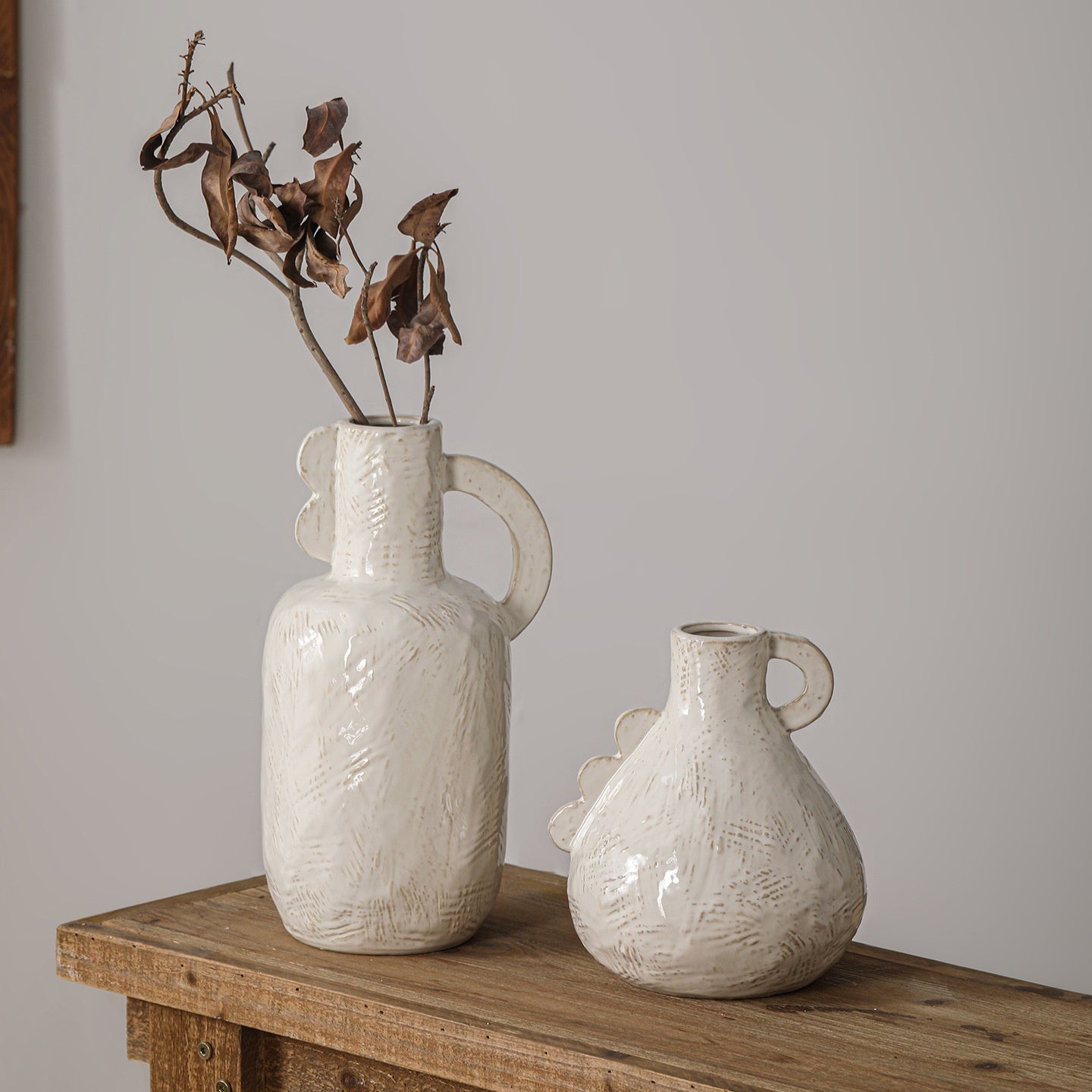 Two white textured vases on a wooden surface with a plain background