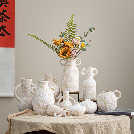 Collection of white textured vases on a table with a floral arrangement against a neutral wall.