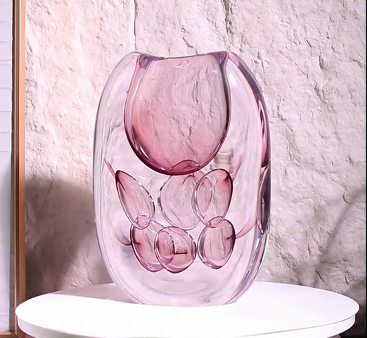 Pink glass vase on a white surface with a textured wall background