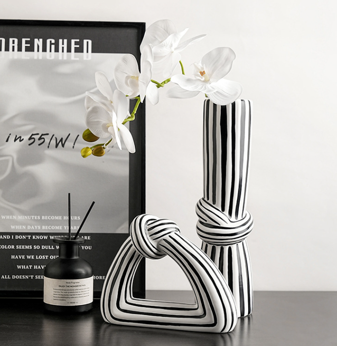 Black and white striped vase with a candle and framed picture on a table