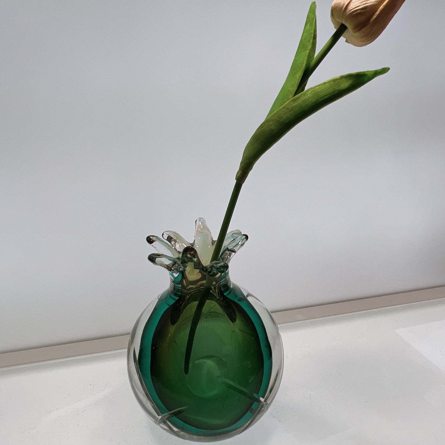 Green glass vase with a single tulip on a white surface