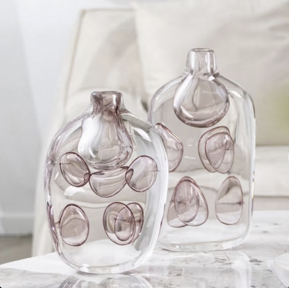 Two clear glass bottles with circular cutouts on a white surface