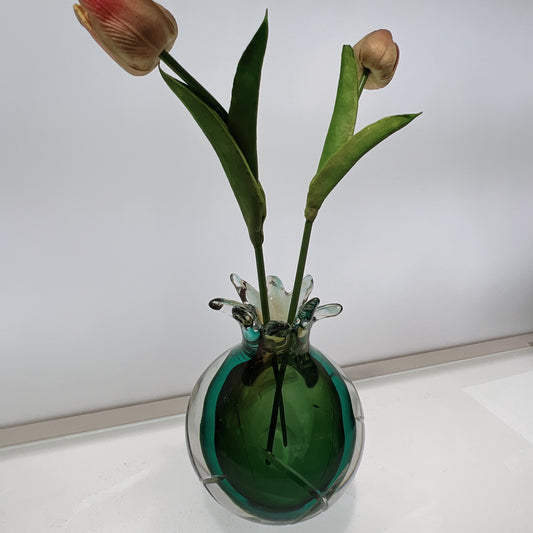 Glass vase with green liquid and tulips on a white surface