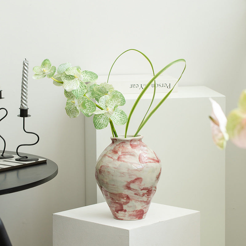 Marble-patterned vase with green plant on a white surface