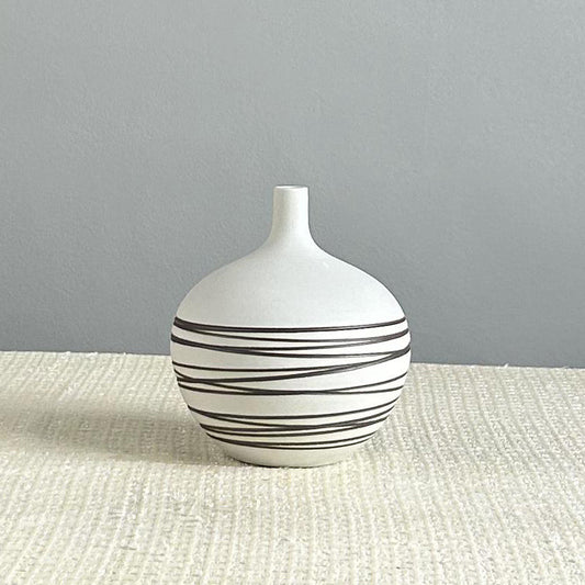 White vase with black stripes on a textured surface and gray background
