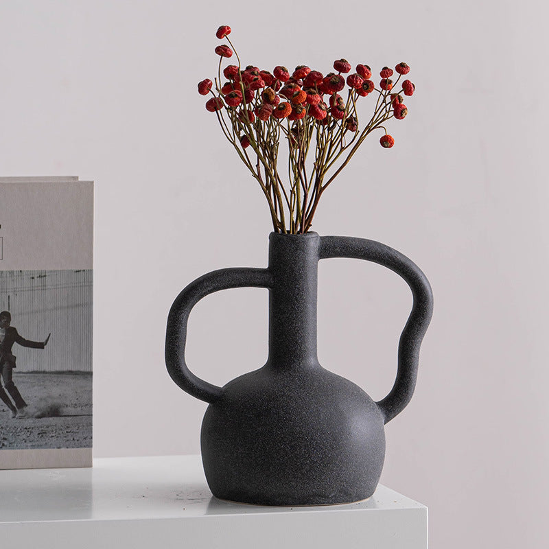 Black ceramic vase with handles holding dried red berries on a white surface.