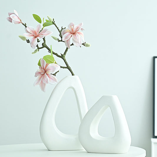 Two white ceramic vases with a branch of pink flowers on a light blue background