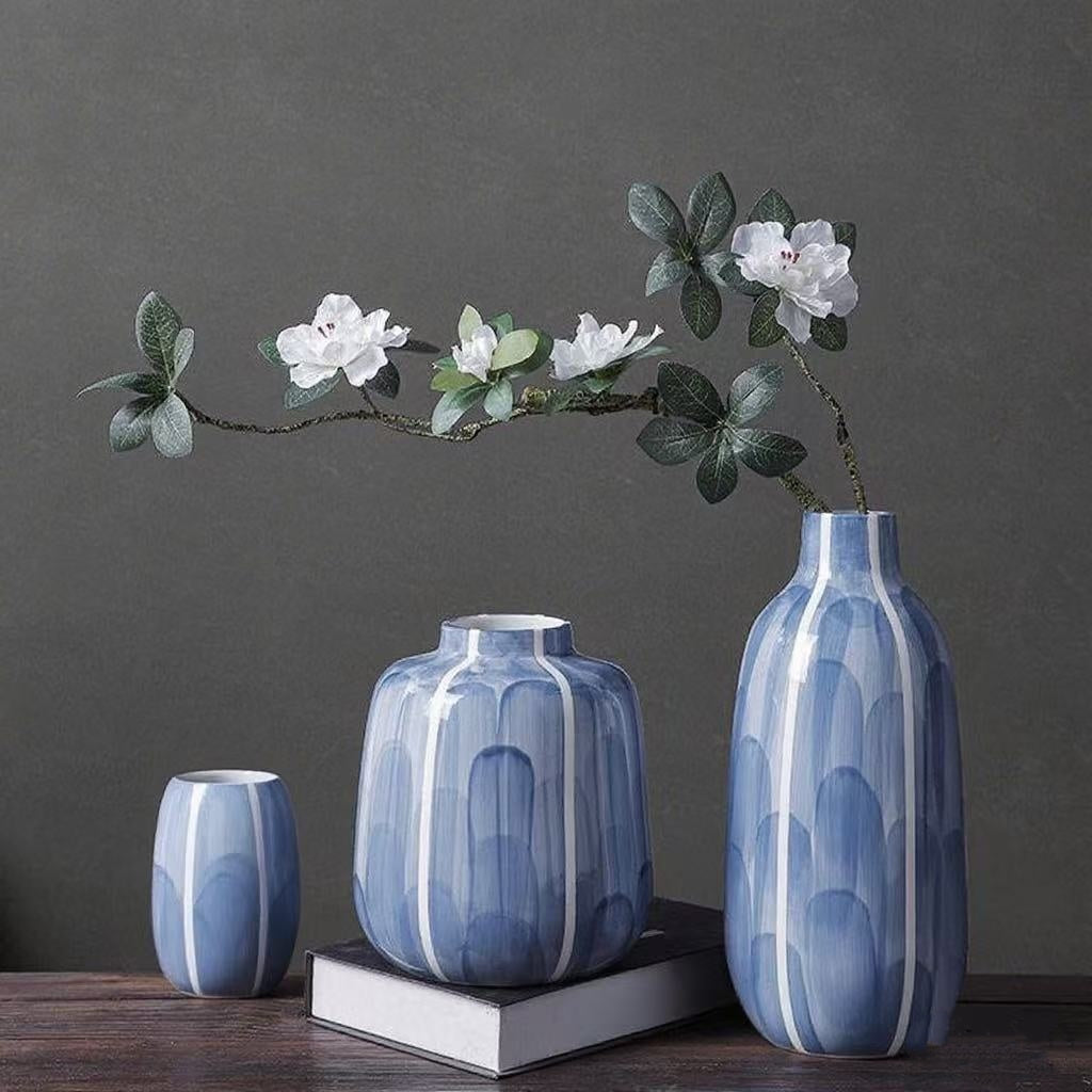 Three blue ceramic vases on a dark surface with a branch of white flowers against a dark background.