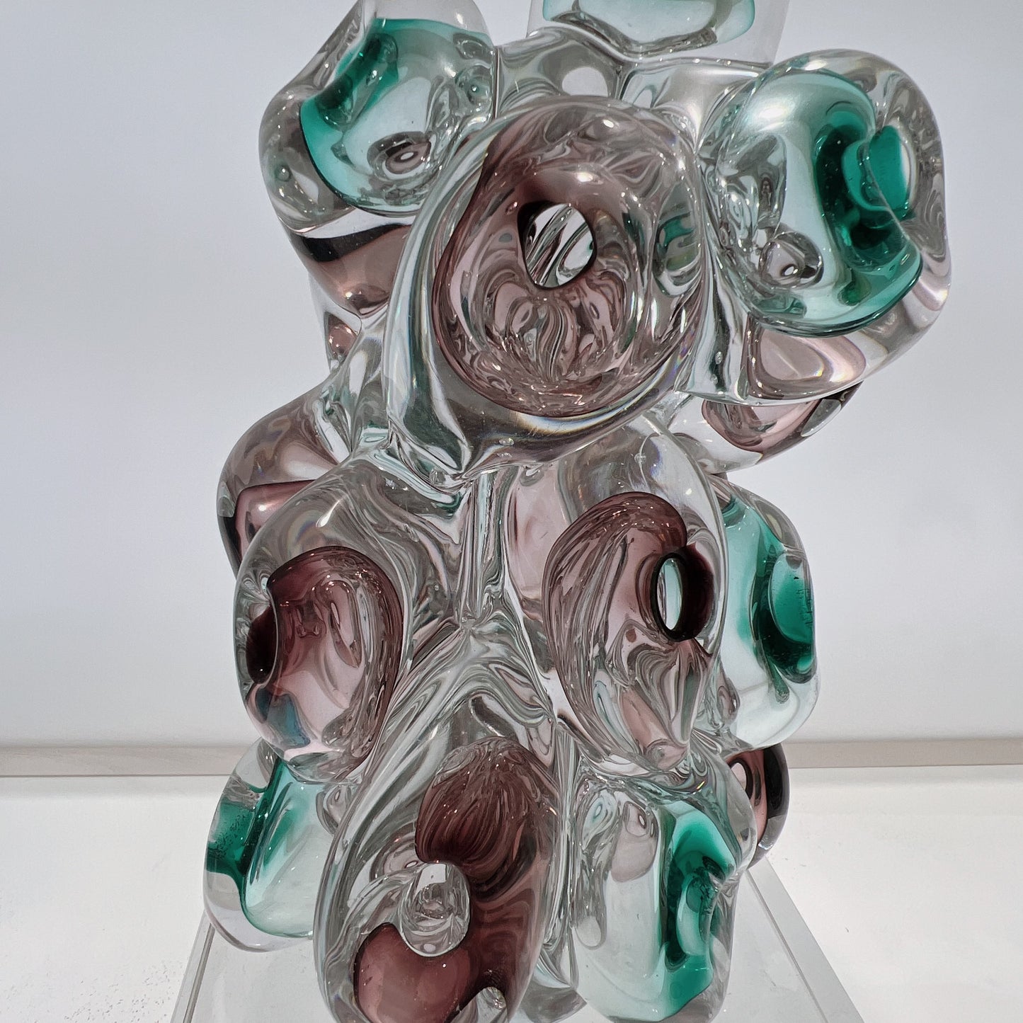 Glass sculpture with swirl patterns in green, brown, and clear on a white background