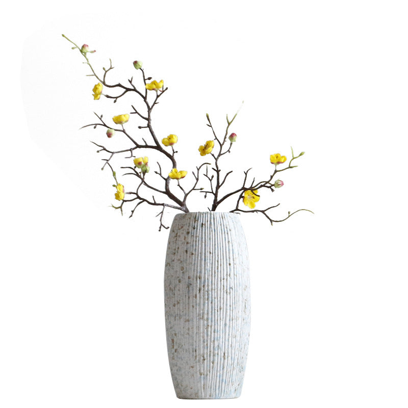 Decorative vase with textured surface holding branches with yellow flowers on a white background
