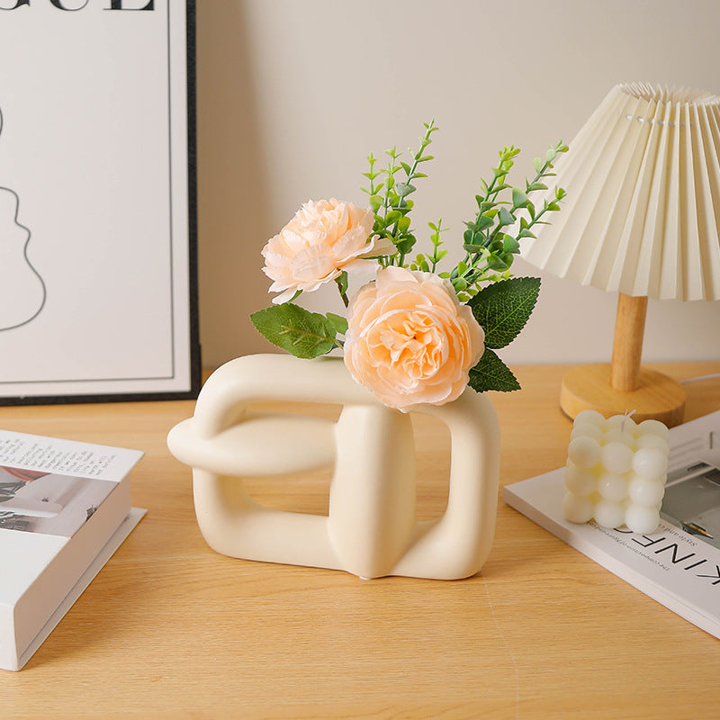 Decorative vase with flowers on a wooden surface next to a lamp and books.