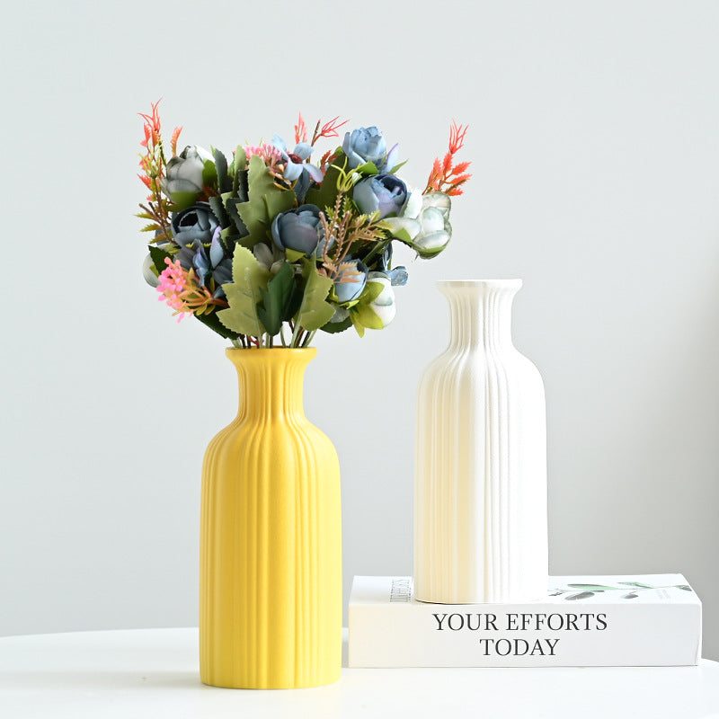Yellow vase with a bouquet of flowers on a white surface with a light gray background