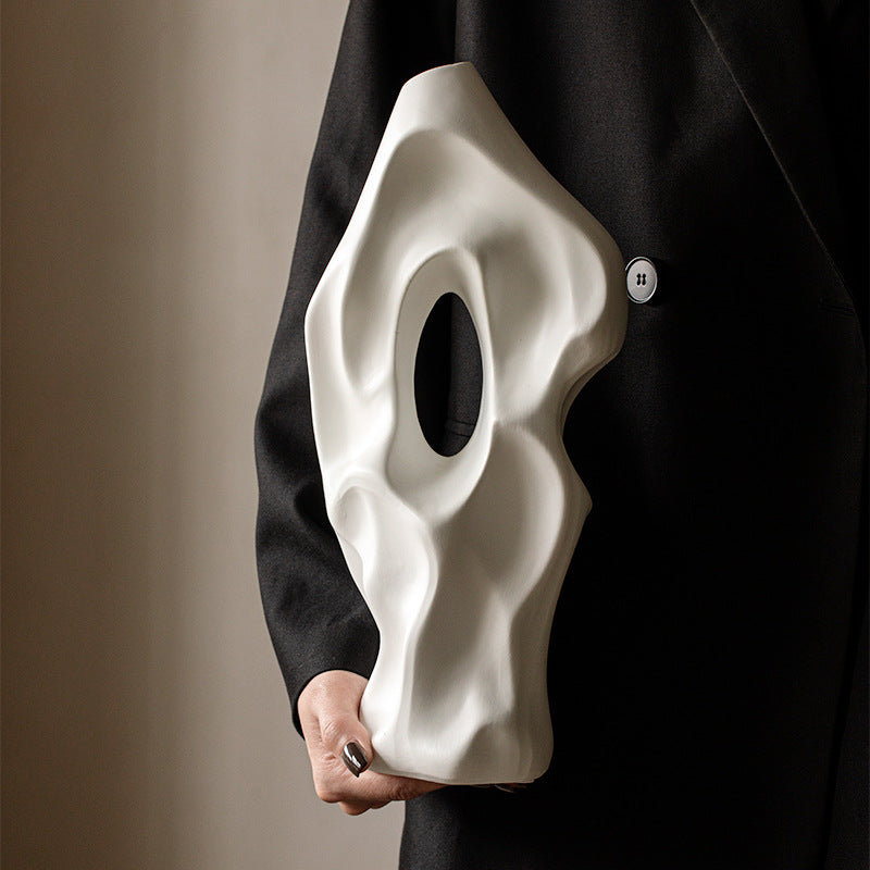 Person holding a white mask against a black coat on a beige background