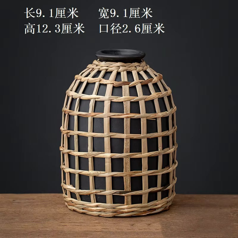 Black vase with woven straw cover on a wooden surface and dark background