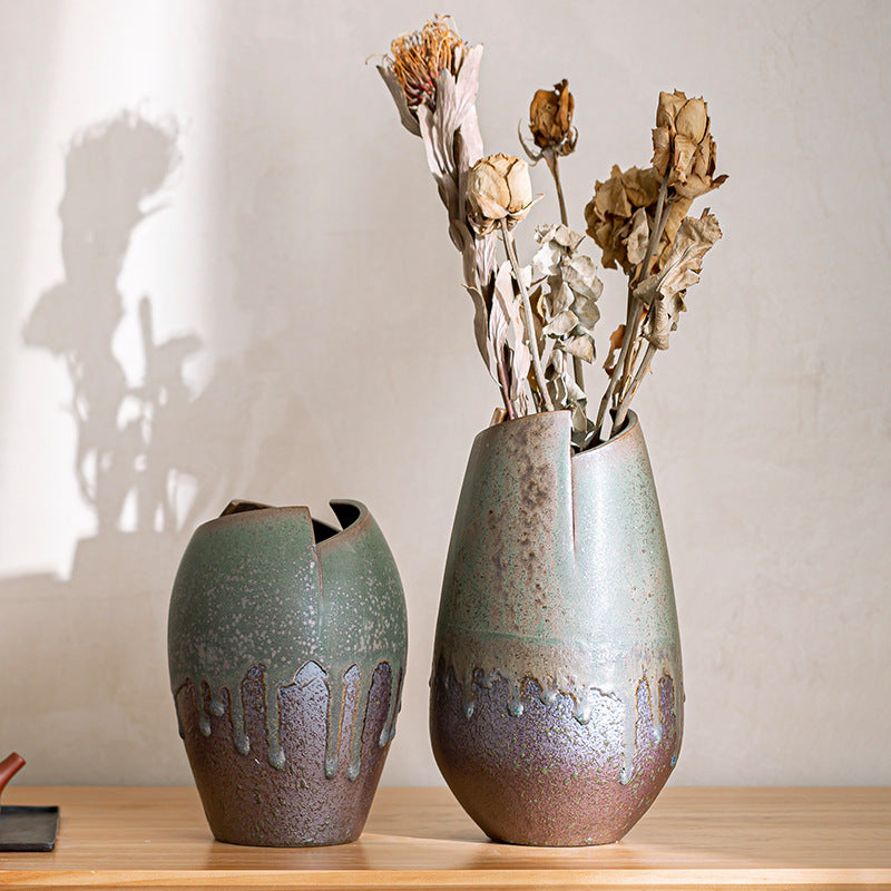 Two ceramic vases with textured finish on a wooden surface, one containing dried flowers.